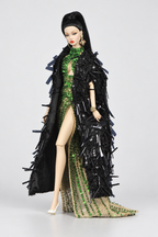 Three-quarter view of a long black embellished doll coat over the emerald gown, showing its broad textured silhouette.