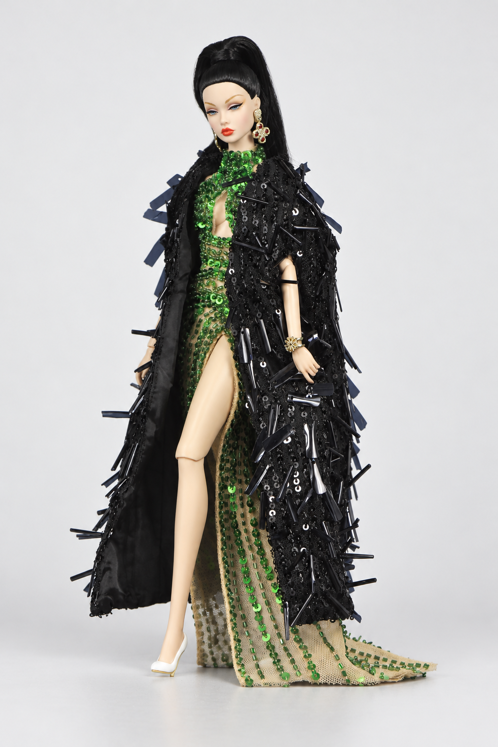 Three-quarter view of a long black embellished doll coat over the emerald gown, showing its broad textured silhouette.