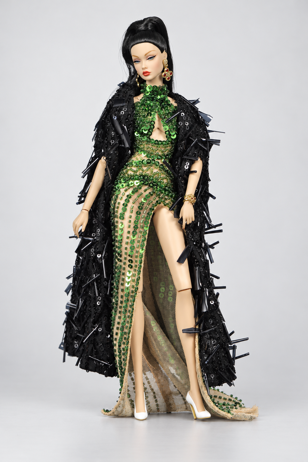 Fashion doll wearing an emerald high-slit gown framed by a long black coat with glossy projecting embellishments.