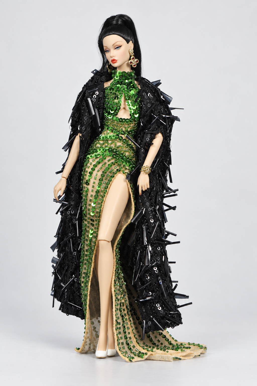 Fashion doll with crossed legs in the emerald beaded gown and long black textured coat worn around the shoulders.