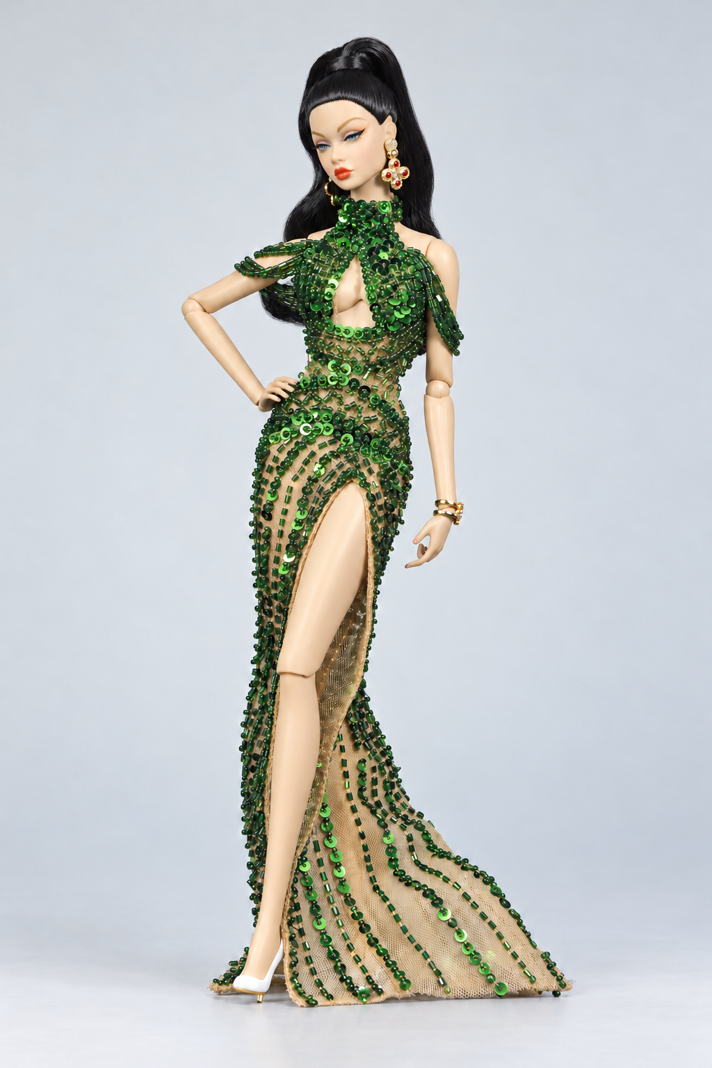 Full-length fashion doll in an emerald embellished keyhole gown with draped shoulder strands, a high slit and sheer train.