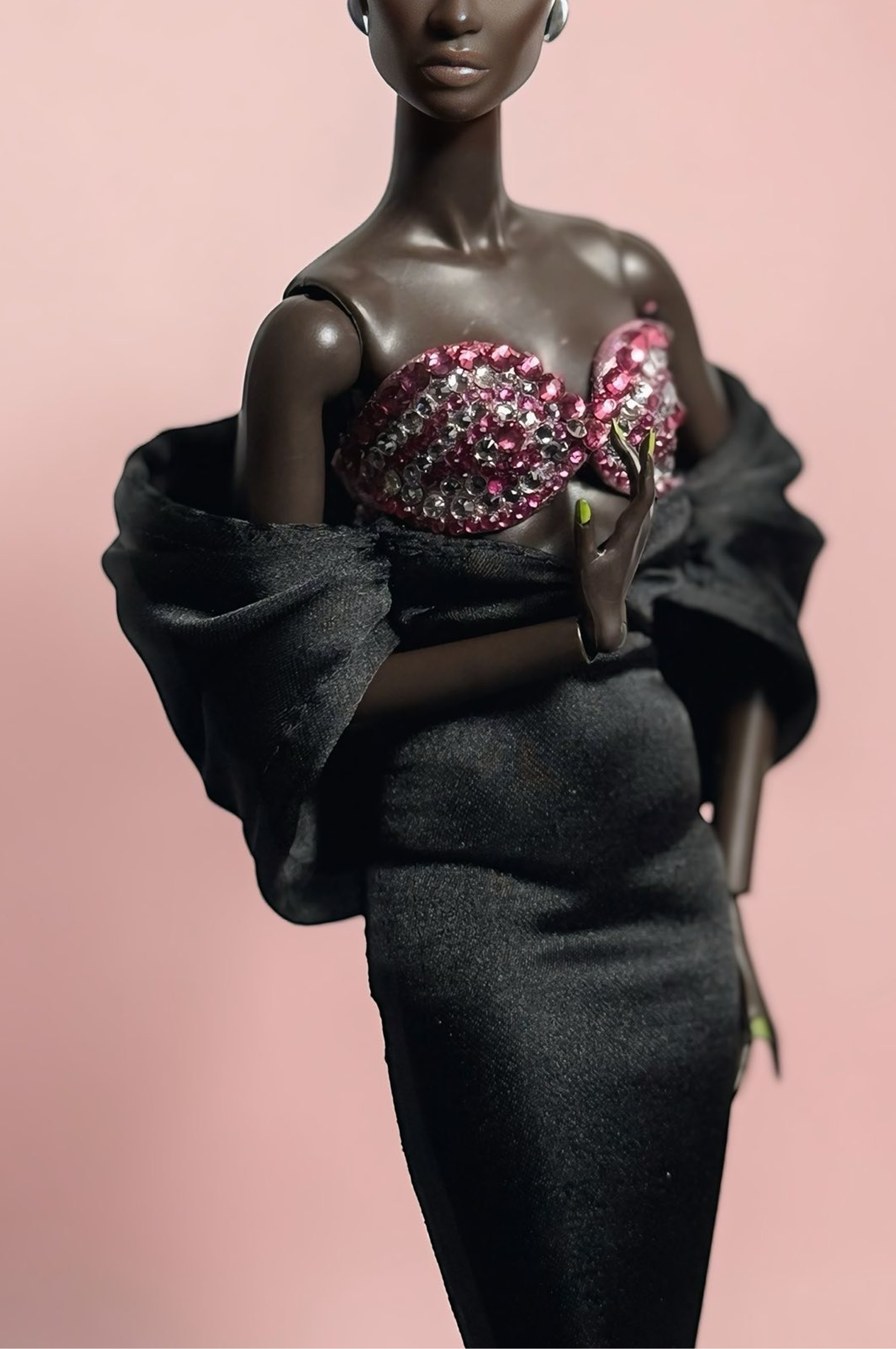 Doll wearing a black dress with a pink embellished top against a pink background