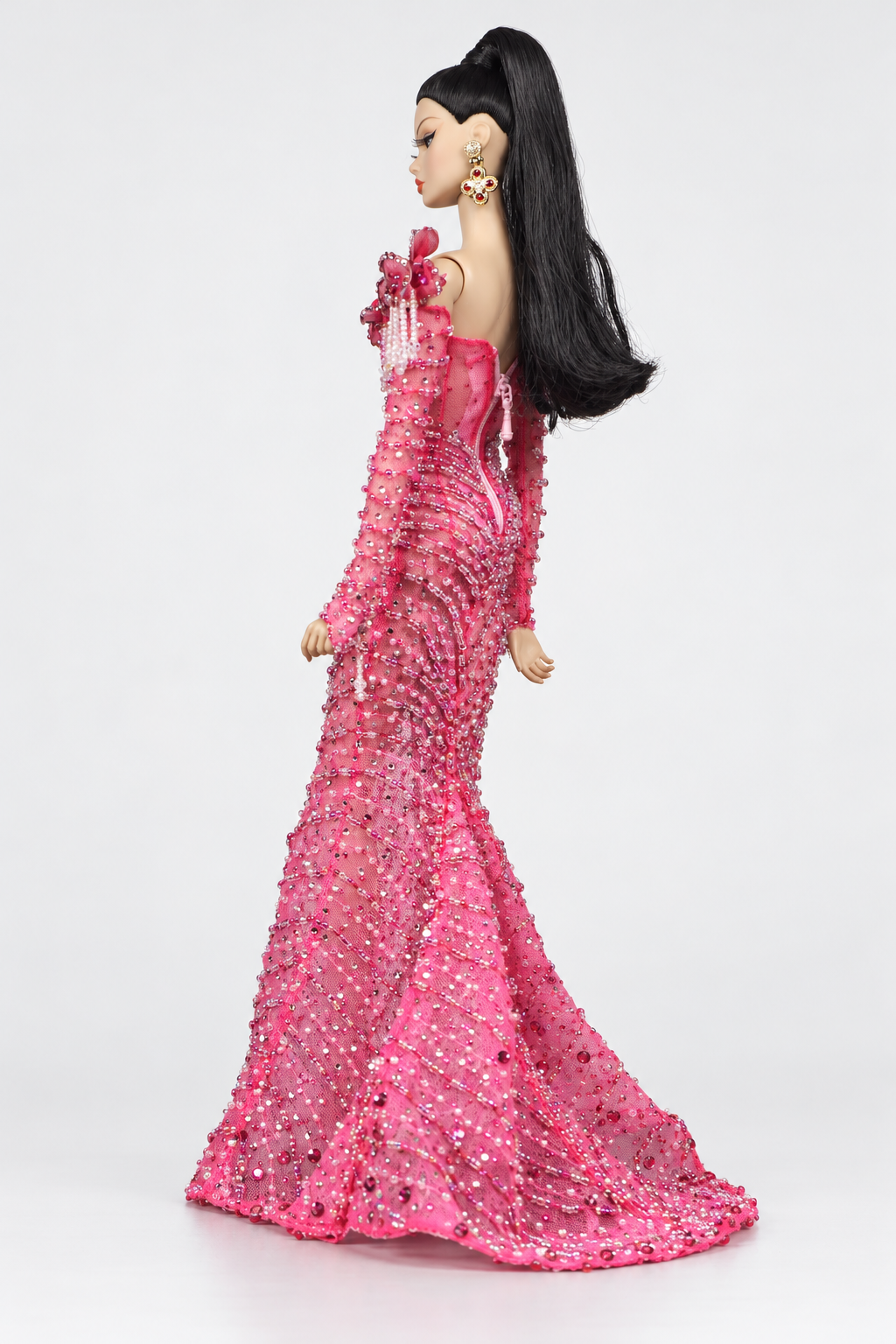 Rear three-quarter view of the pink embellished doll gown with long sleeves, a fitted back and flared train.