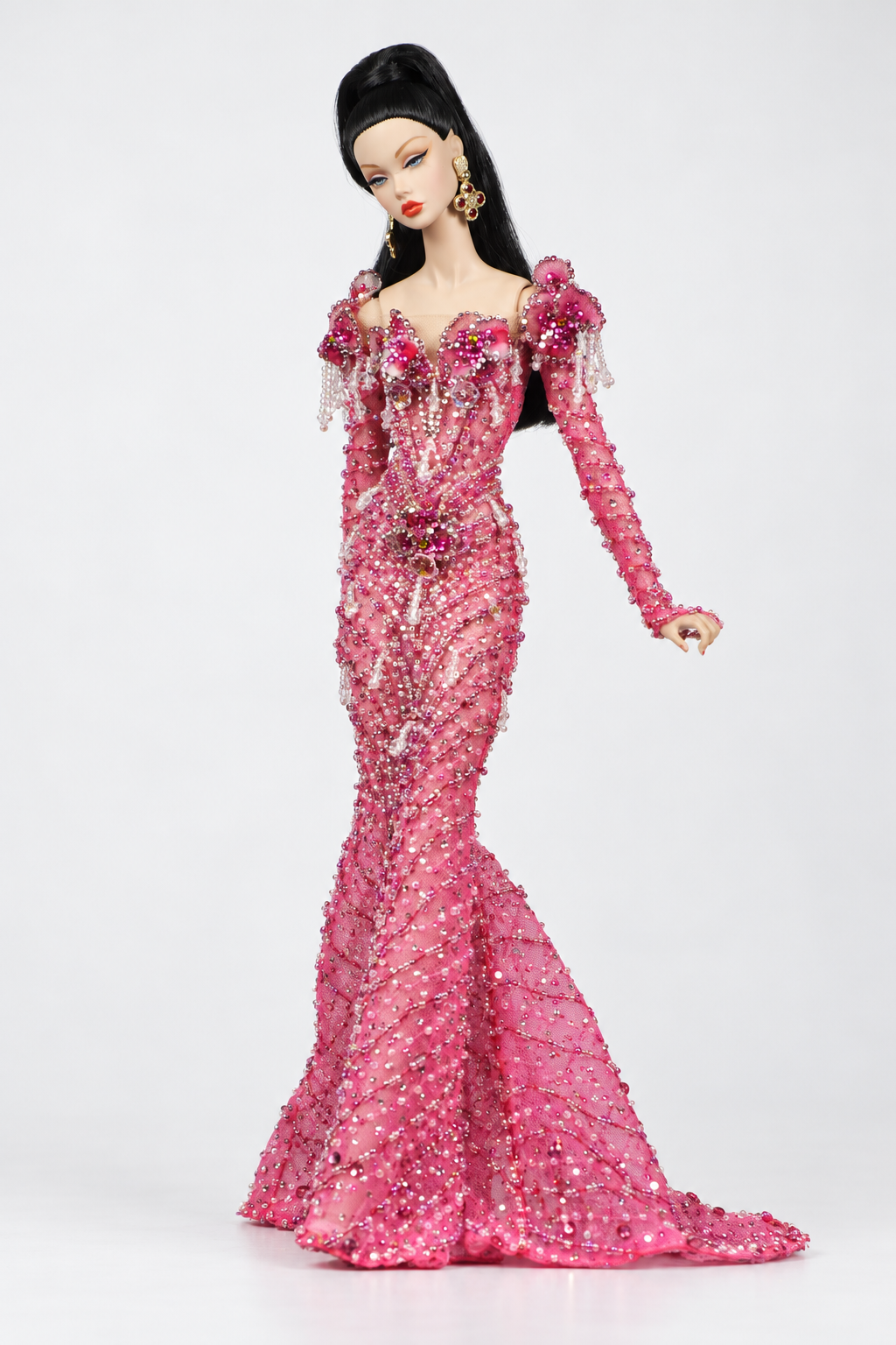 Fashion doll in a pink embellished gown with one arm extended to show the decorated sleeve and floral shoulder.