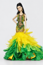 Fashion doll tilts her head while wearing a green and yellow sheer embellished gown with a full feather hem.